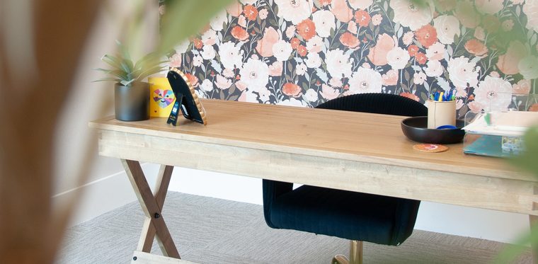 A calm, organized desk with a navy chair against floral wallpaper