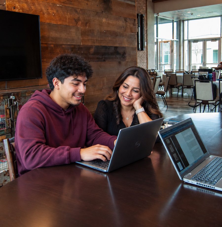 A student and a parent smiling together while working at laptops